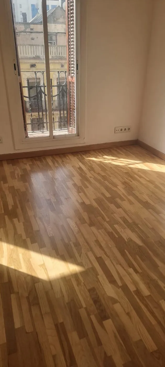 Salón reformado con suelo de parquet y balcón con luz natural